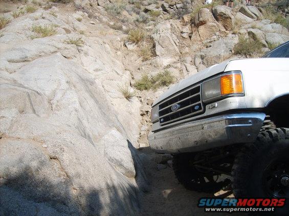 White Ford truck with chrome bumper navigating a rocky off-road trail