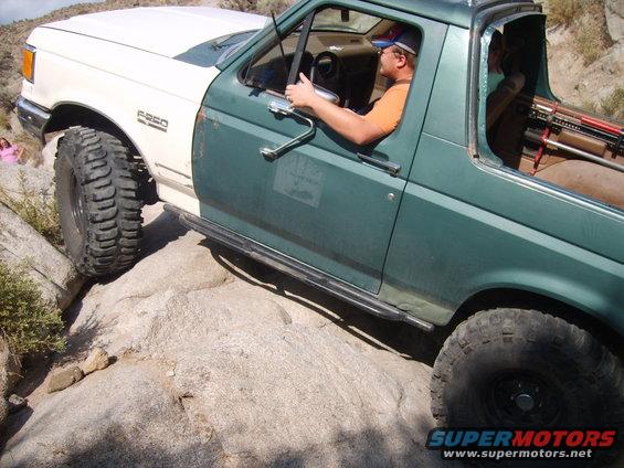 Ford F-250 off-roading over rocks, driver in orange shirt