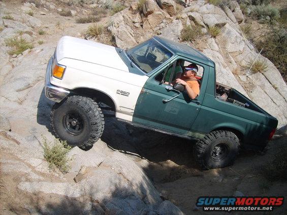 Green and white Ford F-250 truck with off-road tires climbing rocks