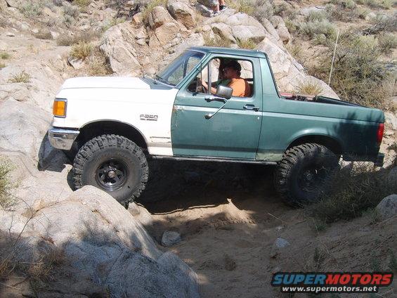 1989 Ford Bronco off-roading on rocks, white front fender, green cab and rear