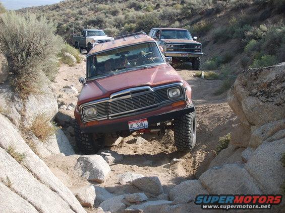 Red Jeep Wagoneer navigating rocky terrain, AL 8341 license plate visible