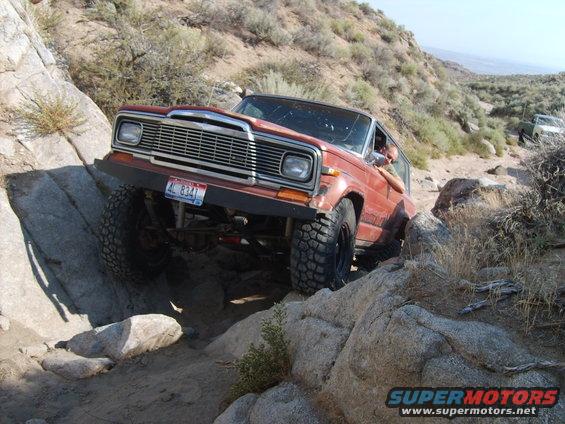 Red Jeep Cherokee Chief navigating a rocky trail, another vehicle visible in background
