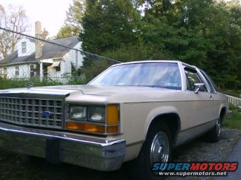 Tan 1986 Ford Crown Victoria LTD sedan, front 3/4 view, parked outdoors near a house