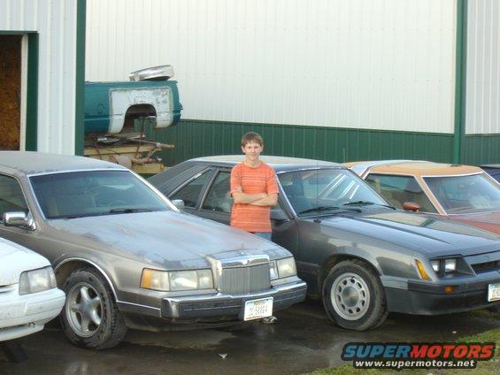 1986 Ford Mustang parked next to a Lincoln and another car, with a person standing between them