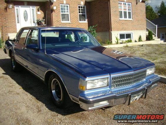Blue sedan parked in front of a brick house, front quarter view