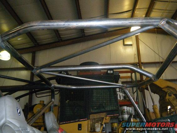 Metal roll cage over gray seats inside a workshop with heavy machinery in the background