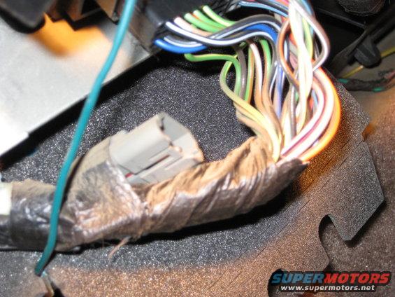 Close-up of a vehicle's wiring harness with multiple colored wires and a gray connector