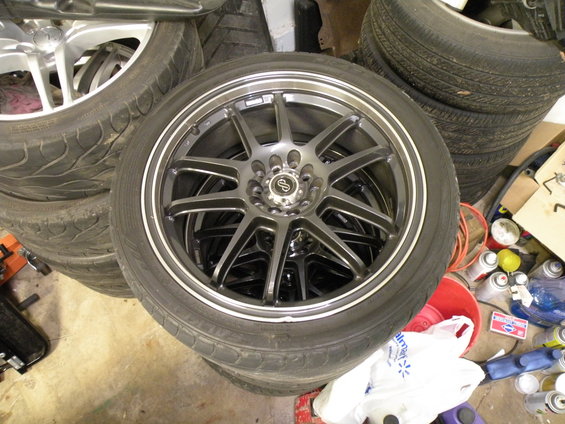 Stack of tires with aftermarket wheels, one in focus