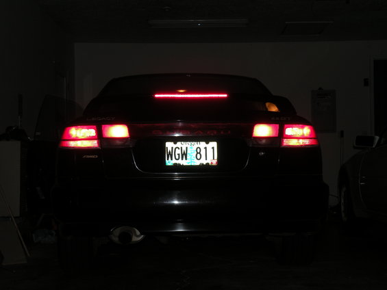 Rear of a black Subaru Legacy with brake lights on. License plate reads WGW 811