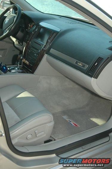 Interior shot of a car's dashboard, center console, and passenger seat. Shows wood trim, infotainment screen, and floor mats