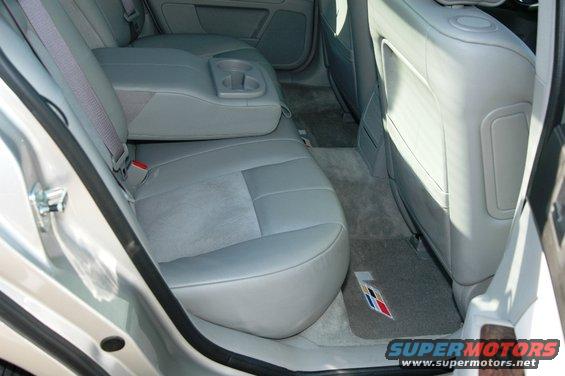 Silver car interior with gray leather seats, rear armrest with cup holders, and a floor mat with a colorful emblem