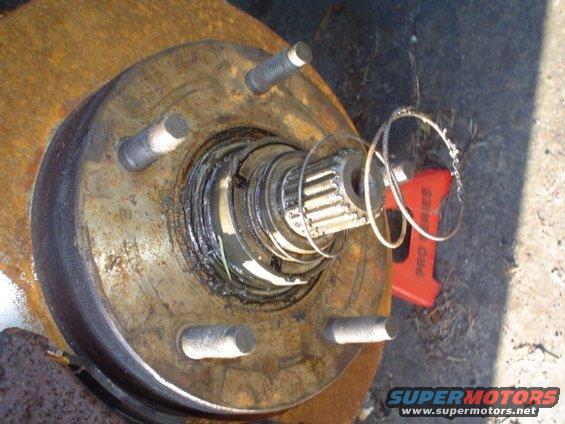 Close-up of a rusty wheel hub assembly with splined axle shaft and brake rotor. A red 'PRO SERIES' tool is visible in the background