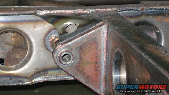 Welded steel frame bracket with circular cutouts and bolt holes, showing heat discoloration