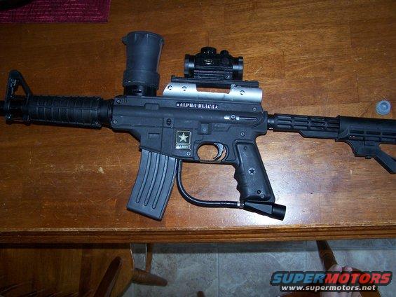 Black paintball gun with "ALPHA BLACK" and "U.S. ARMY" markings, on a wooden table