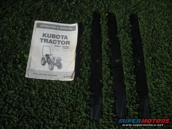 Kubota tractor operator's manual and three black mower blades on grass