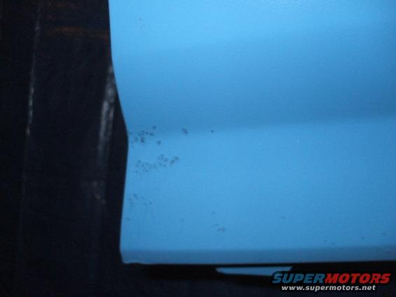 Close-up of a blue vehicle's side panel showing small rust spots forming near the edge
