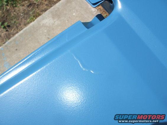 Blue painted metal panel with a dent and a 'SUPERMOTORS' watermark