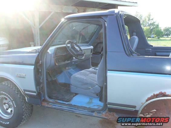 Side view of a 1990 Ford Bronco with the driver's door open, showing the interior