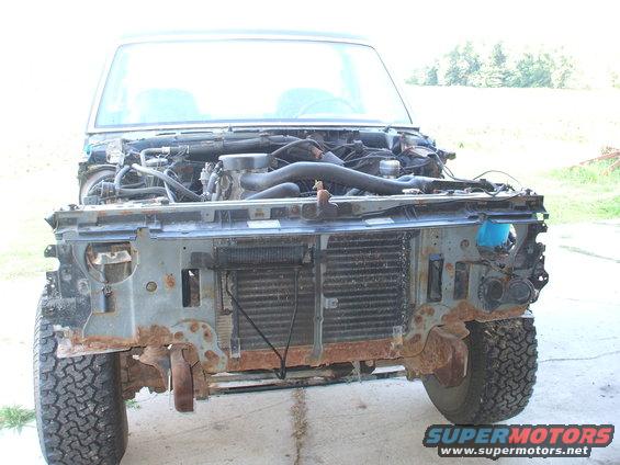 Front of a Ford Bronco with hood removed, showing engine and radiator. Body is rusty