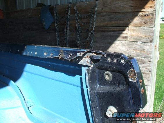 Close-up of a rusted blue and black vehicle body panel with visible bolt holes and damage
