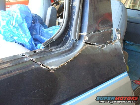 Dark blue and gray vehicle interior with blue tarp covering seats and rusted, cracked door frame