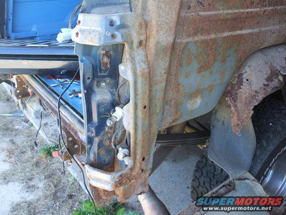 rusted blue vehicle body panel with exposed wiring and tire visible