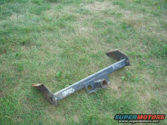 Black trailer hitch with "HIDDEN HITCH" text, lying on grass