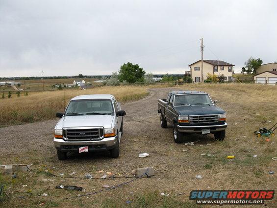 1999 Ford F-250 and an older Ford truck parked on a gravel driveway with houses in the background