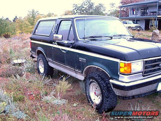 1989 Ford Bronco parked on a dirt lot with dry brush