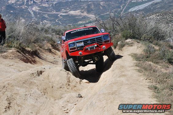 Red Ford Bronco with winch on front bumper navigating a steep dirt trail, website www.fulizebronco.com on windshield