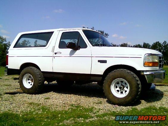 White 1995 Ford Bronco parked on gravel with grass and trees in background