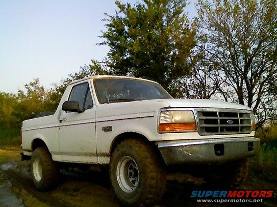 White Ford Bronco with off-road tires on muddy terrain, front 3/4 view