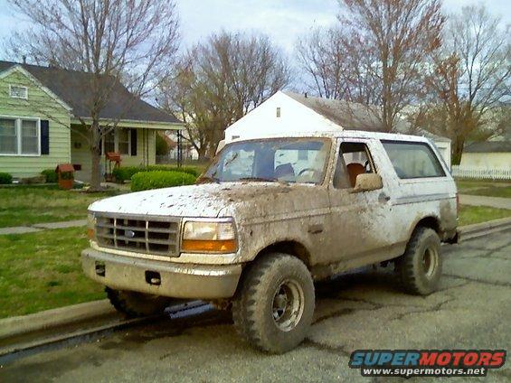 1995 Ford Bronco covered in mud, parked on a residential street