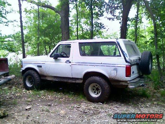 White 1992 Ford Bronco with a spare tire mounted on the rear, parked on a dirt path in the woods