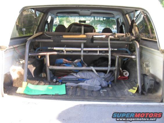White SUV interior with roll cage, camping gear, and a green mat on the floor