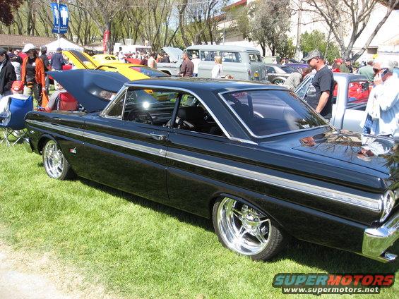 Black coupe with chrome side trim and custom wheels parked on grass