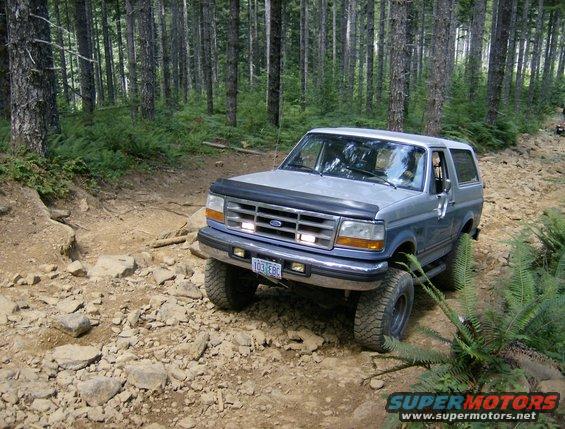 blue and silver 1996 Ford Bronco drives on a rocky, wooded trail