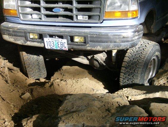 Front of a blue Ford truck with its tires on rocks and dirt