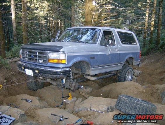 Two-tone blue and gray Ford Bronco with lifted suspension, off-roading in a forest