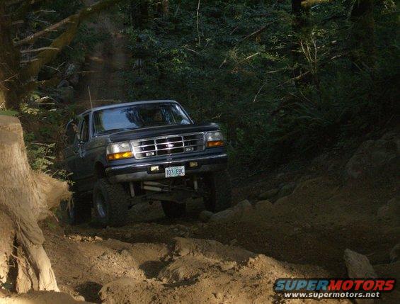 Dark blue Ford Bronco off-roading on a dirt trail, front 3/4 view
