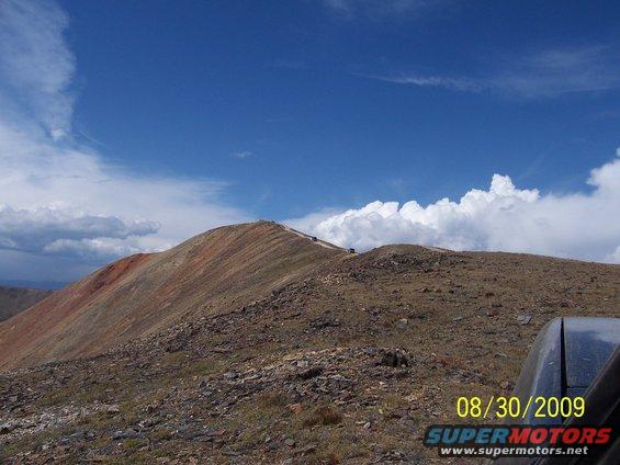 Off-road vehicles driving on a mountain ridge under a blue sky with clouds