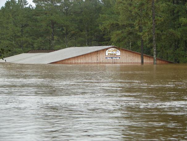Building submerged in floodwaters, with trees in background. Sign reads 'Sun Valley Stables'