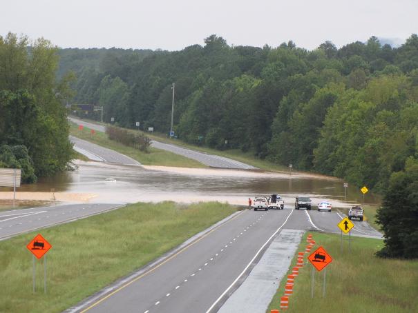 Flooded highway with several vehicles stopped, including white pickup trucks and a dark SUV