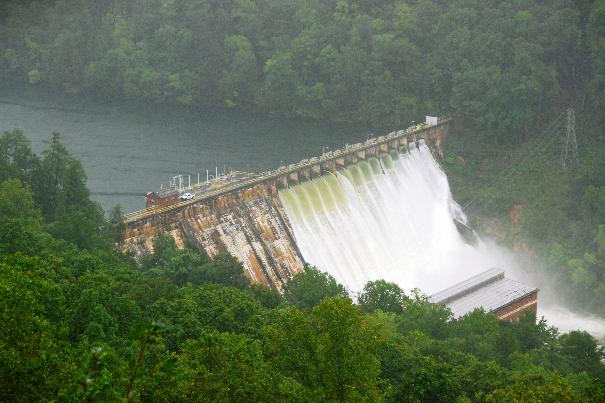 Dam with water cascading down, a white car is visible on the dam's crest
