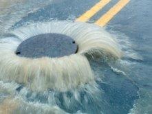 Water gushing out of a manhole cover on a flooded street with double yellow lines