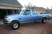 1995 Ford Bronco - A light blue pickup truck is parked in front of a garage with a white truck behind it.