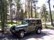 2002 Jeep TJ - A green Jeep TJ is parked in a driveway surrounded by pine trees, with a house in the background.