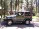 2002 Jeep TJ - A green 2002 Jeep TJ Wrangler with a brown soft top is parked outdoors among trees.