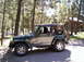 2002 Jeep TJ - This 2002 Jeep TJ Wrangler is seen in a wooded area, likely a campsite, with a cabin visible behind it.