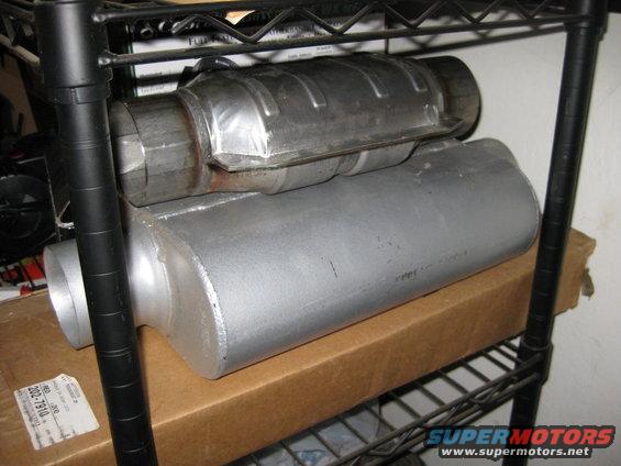 Two metal exhaust components, one a catalytic converter, stacked on a shelf